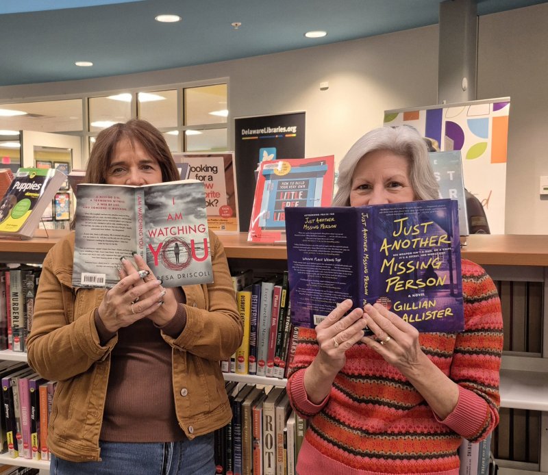Friends of the Lewes Public Library volunteers Joni Thorne, left, and Kathy Burdon get into the spirit while showing off two of the thousands of titles that will be available at the mystery and fiction book sale Jan. 23-24. SUBMITTED PHOTO